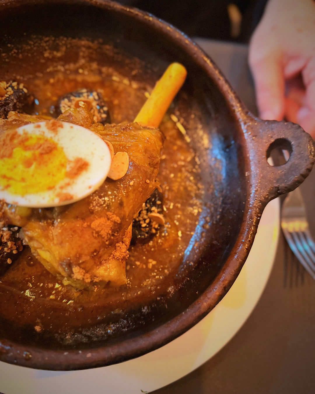 Een mals lamsschenkel uit de tajine met halve ei, kaneel en paprika, pruimen en amandelen, aan tafel geserveerd bij Tafilalet